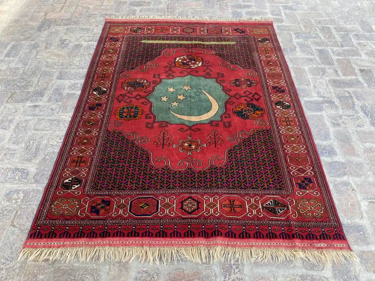 Unique hand-knotted Turkmen rug with rich red background, intricate geometric patterns, and a central green medallion, measuring 5.4 feet by 6.9 feet.