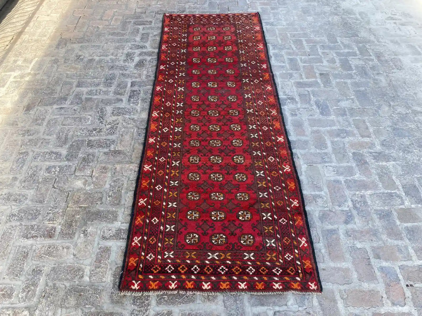 "Hand-knotted Afghan Bokhara rug runner with a rich red background and intricate black and beige motifs, measuring 4'0" x 11'3